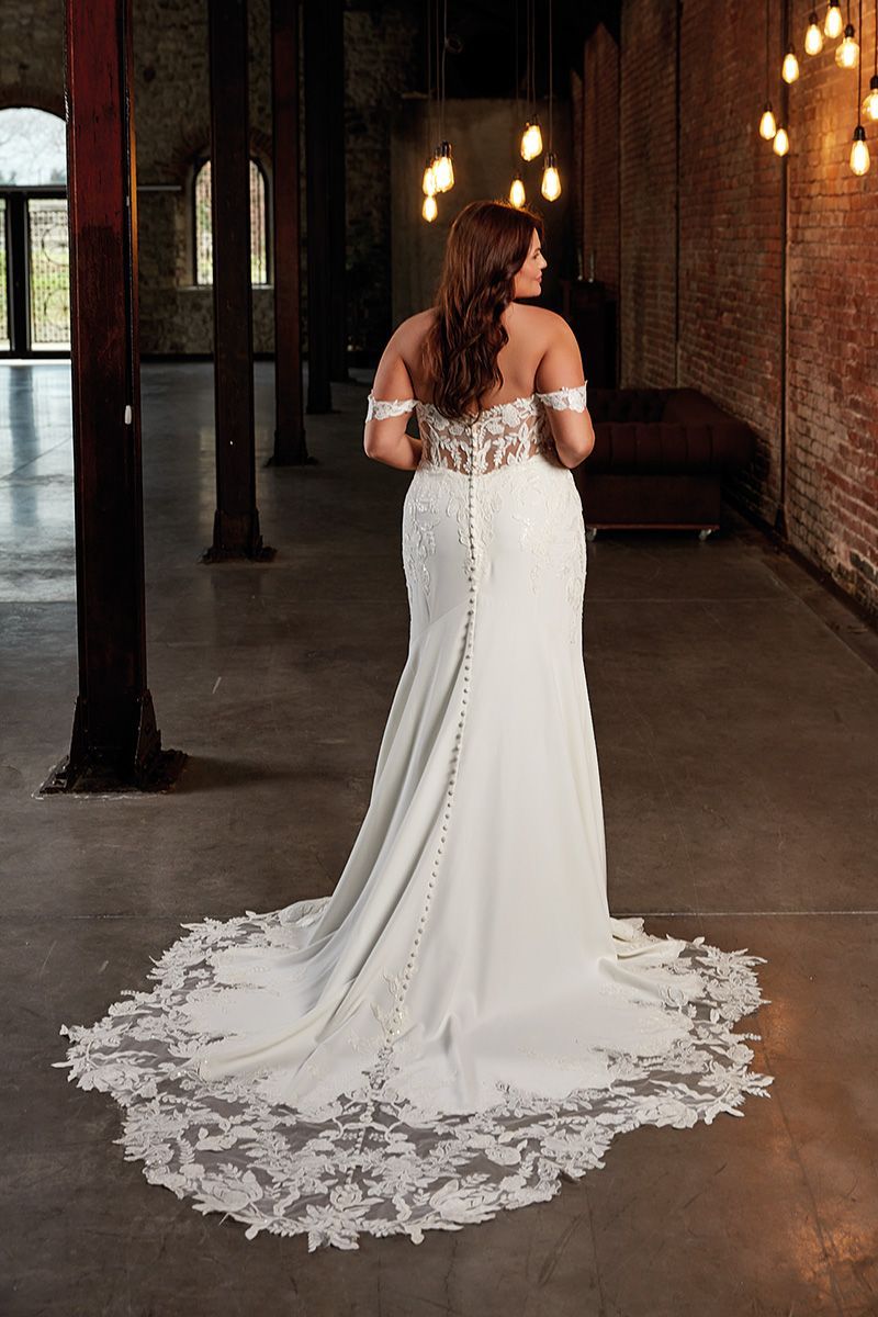 Woman in a white off-the-shoulder wedding gown with a long train, in an industrial setting.