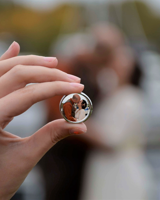 Hand holding a small glass sphere reflecting a couple in wedding attire outdoors