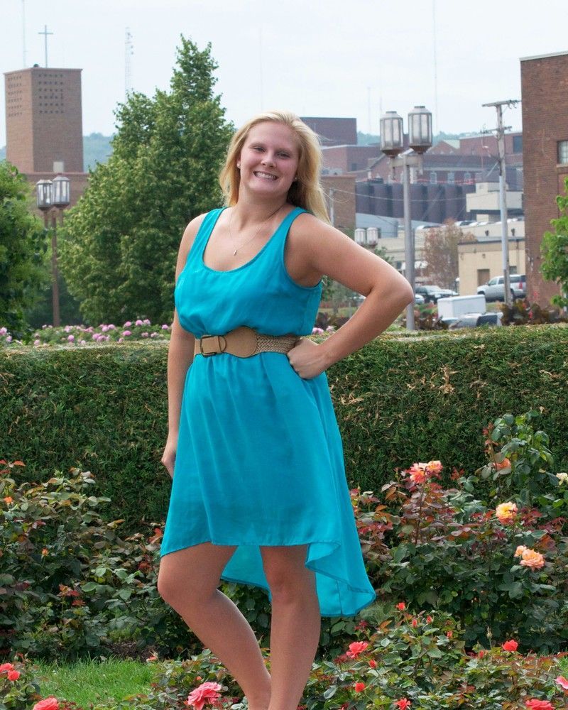 Woman in a turquoise dress posing in a garden with city buildings in the background.