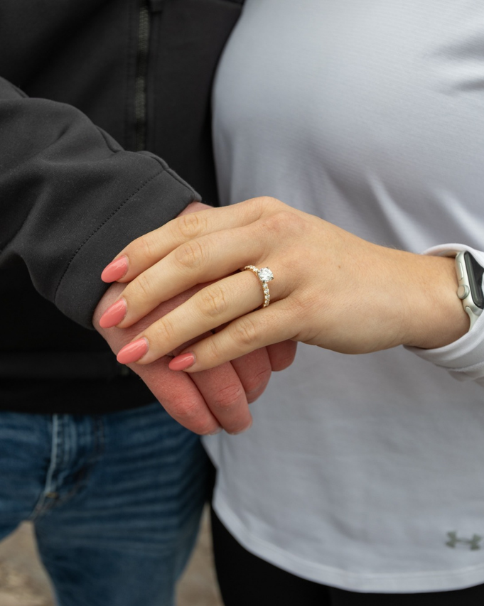 Two people holding hands, one wearing a ring and a white top, the other in a black jacket.