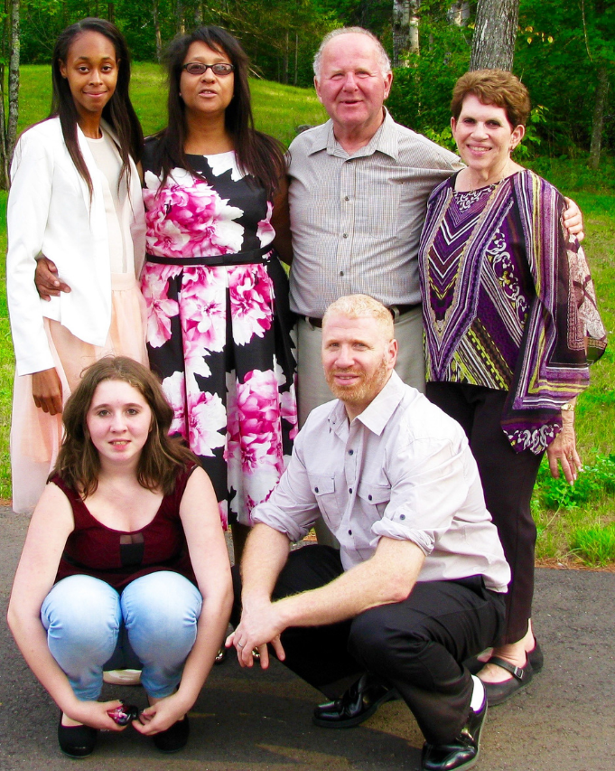 Six people posing outdoors in a garden, with four standing and two crouching in front.