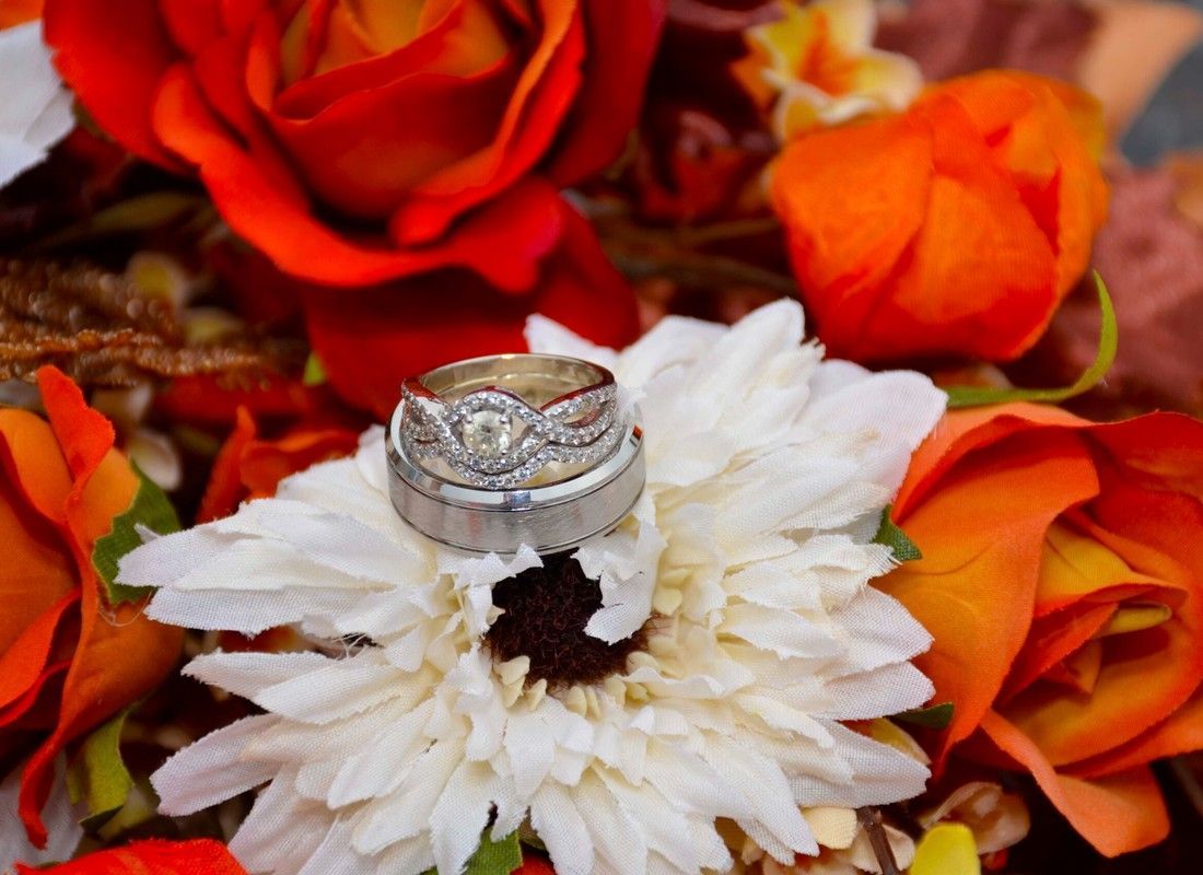 Wedding rings on a white flower surrounded by red, orange, and yellow blossoms