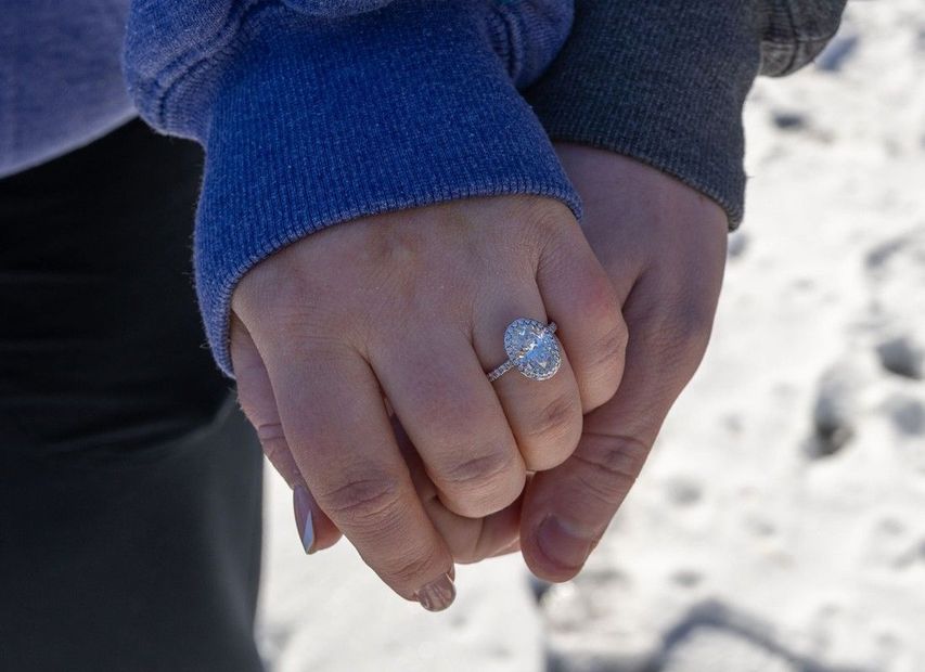 Two hands clasped in a snowy setting, one wearing a diamond ring.
