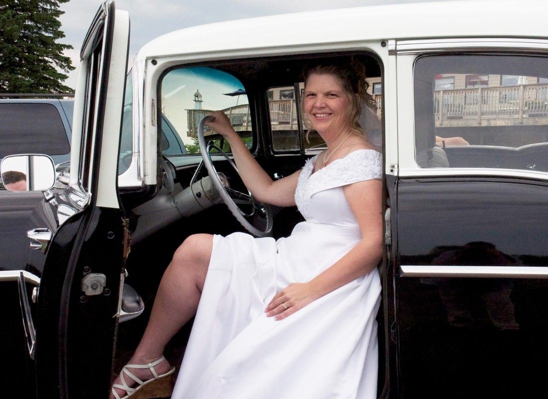 Woman in white dress smiling while sitting in a vintage car with the door open