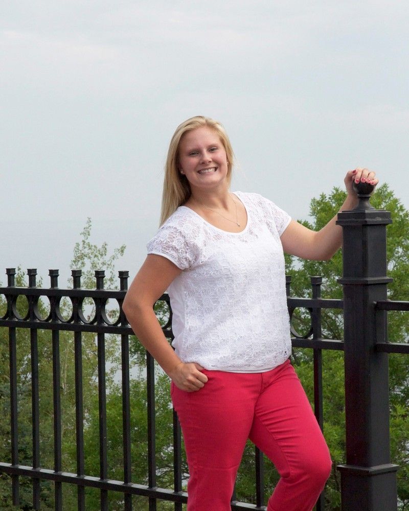 Smiling woman in a white top and red pants posing by a black fence outdoors