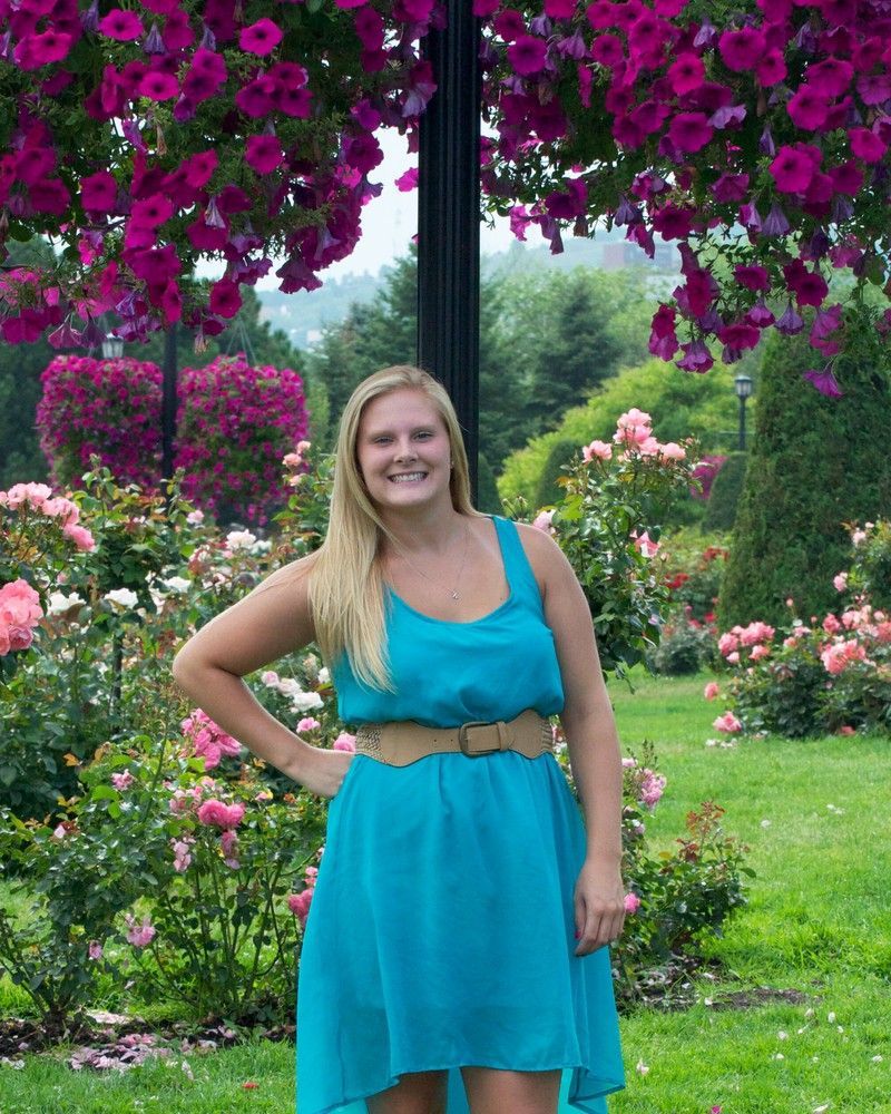 Woman in a turquoise dress standing in a colorful flower garden under pink hanging blooms