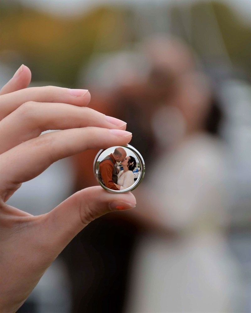 Hand holding a clear glass sphere reflecting a couple at an outdoor wedding ceremony