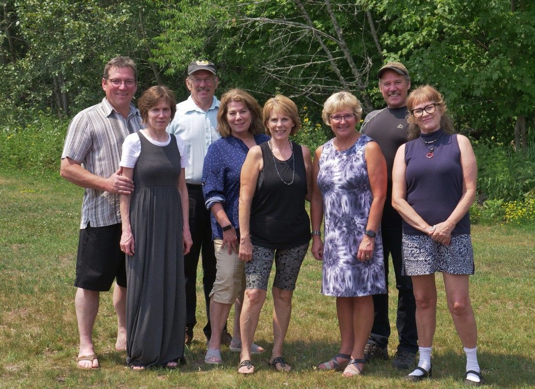 Group of seven people standing together outdoors in a grassy yard with trees in the background