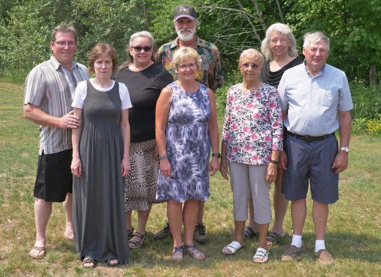 Eight people standing outdoors on grass, posing for a group photo.