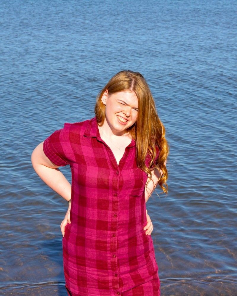 Smiling person in a magenta plaid dress standing by the water