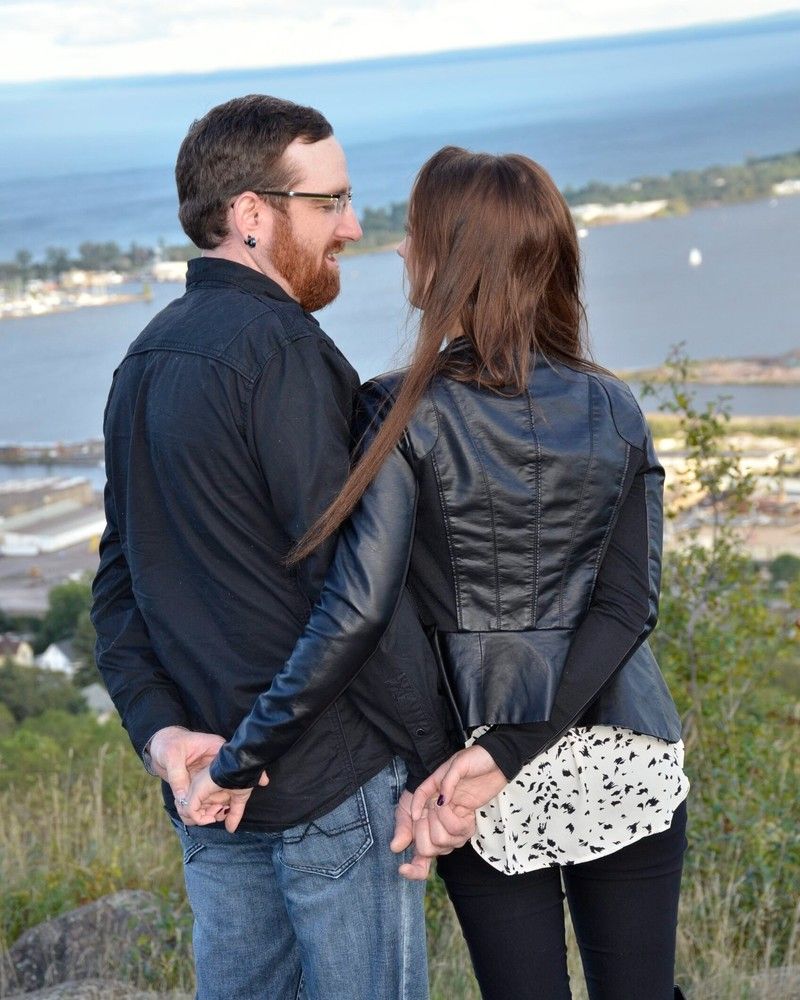 Couple holding hands while looking over a coastal landscape from a hillside.