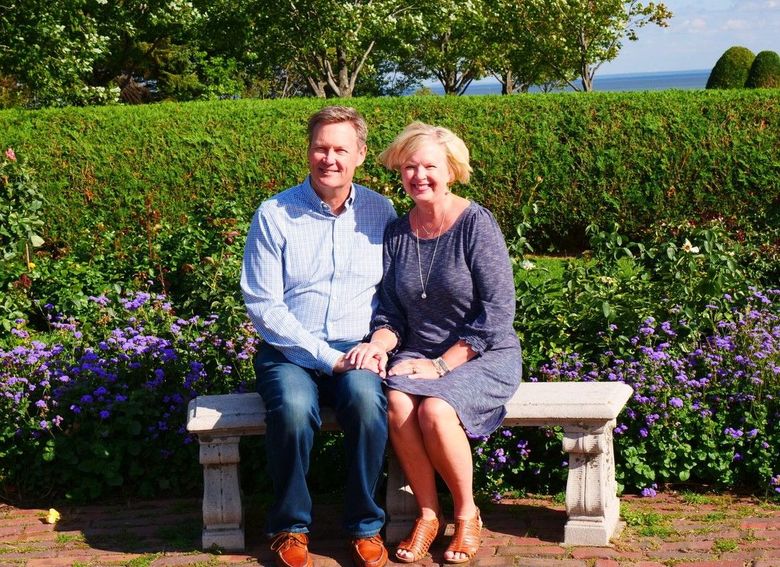 Couple sitting on a white bench in a sunny garden with purple flowers and green hedges