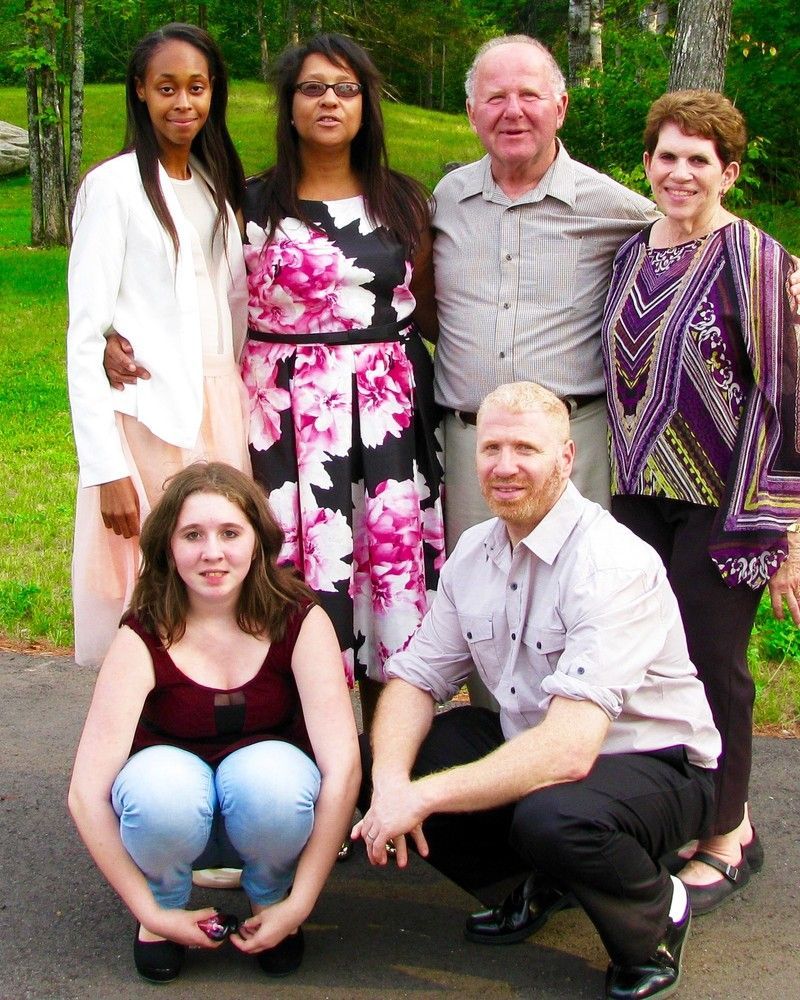 Six people posing outdoors, with two seated in front and four standing behind them.