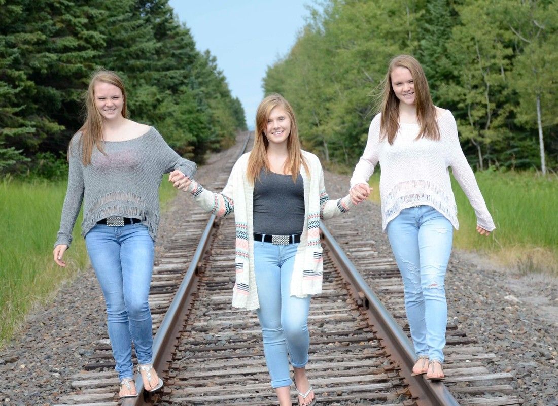 Three people walking along railroad tracks in a green rural area, smiling at the camera.