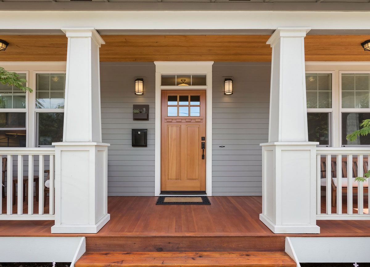 The front porch of a house with a wooden door and a white railing.