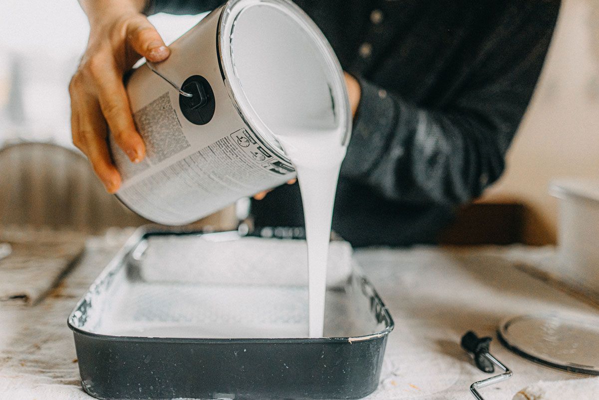 A person is pouring white paint into a tray.