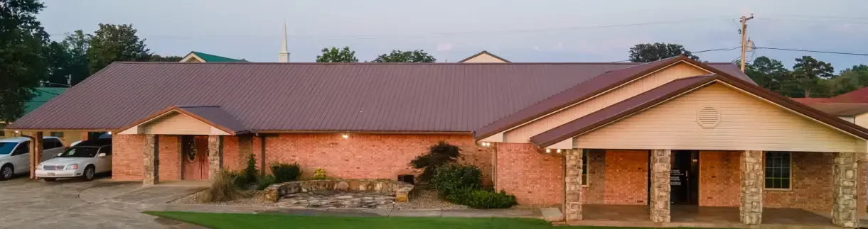 A wide, one-story brick building with a dark metal roof, stone pillars, and two covered porch areas.