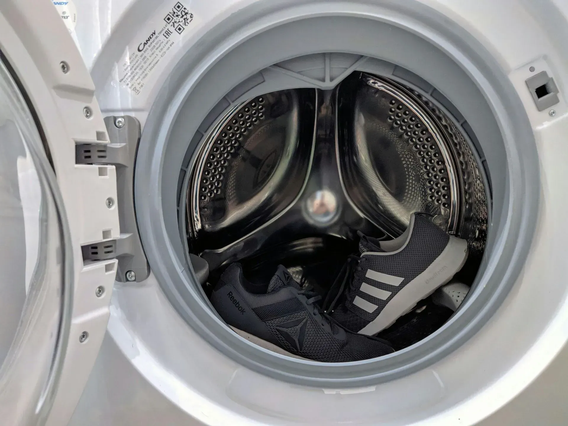 Shoes inside a washing machine, drum is stainless steel, machine is white.