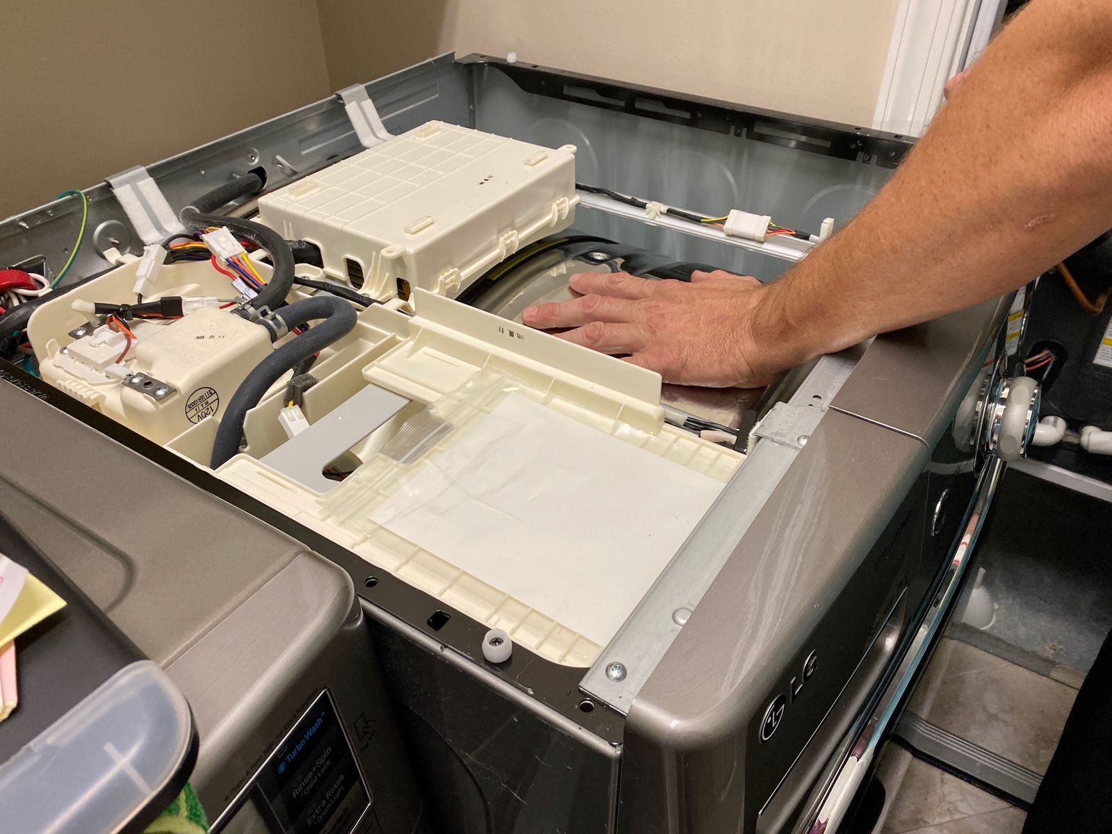 Person's hand on the interior of a disassembled washing machine, likely for repair.