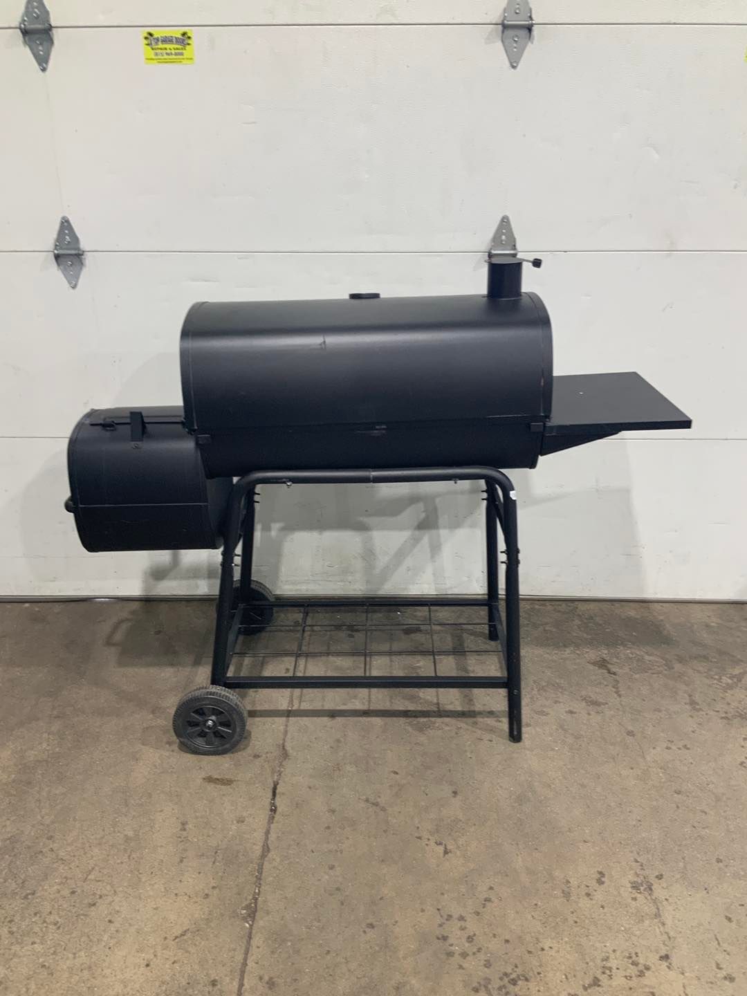 A black grill is sitting in front of a garage door.