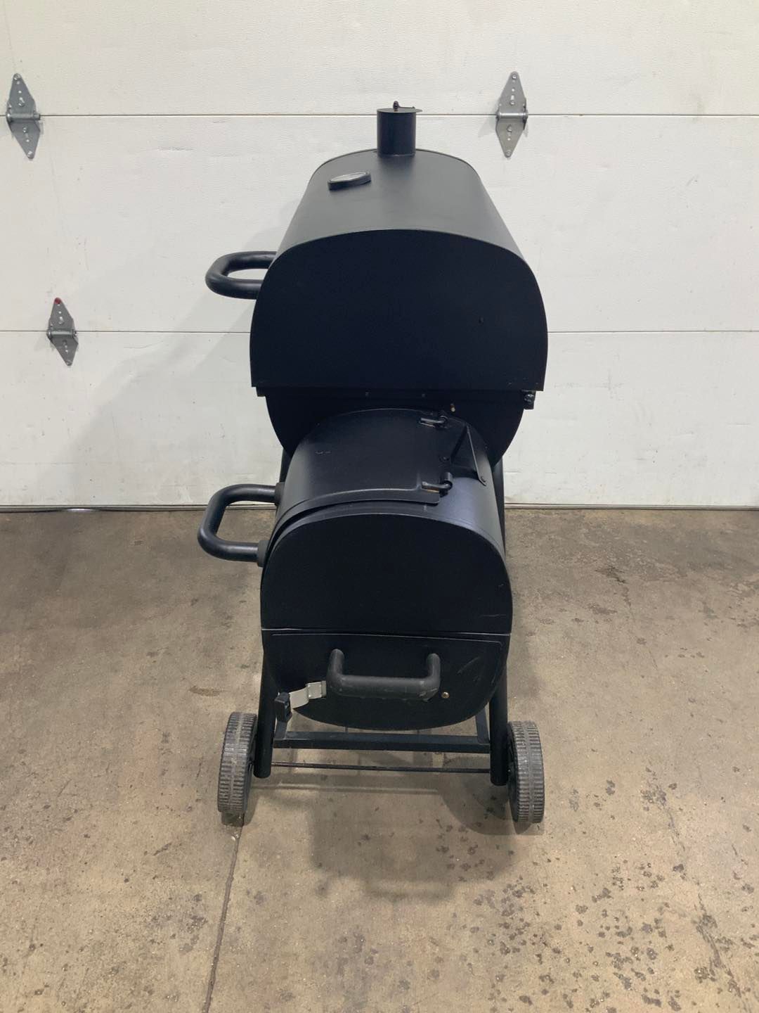 A black grill with wheels is sitting in front of a garage door.