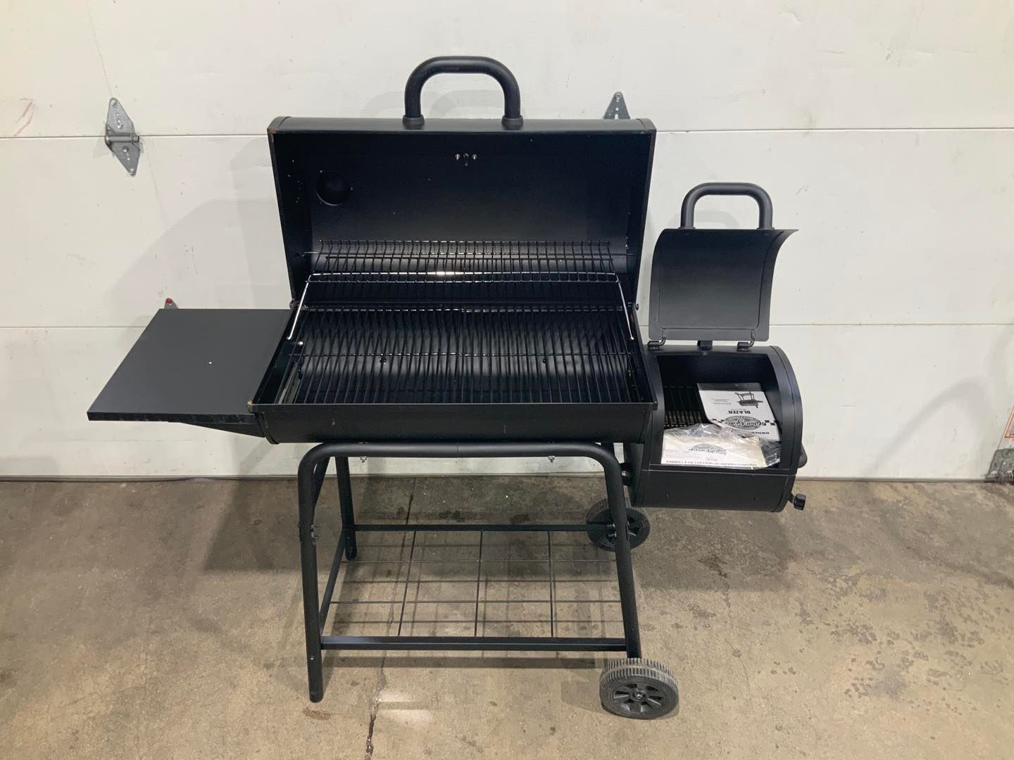 A black grill is sitting on a concrete floor in front of a garage door.
