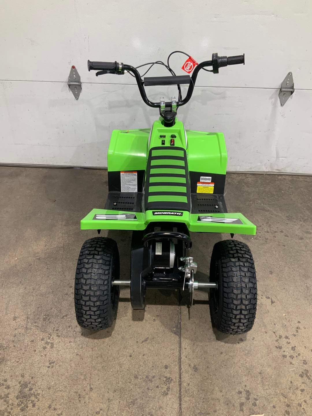 A green atv is parked in front of a garage door.