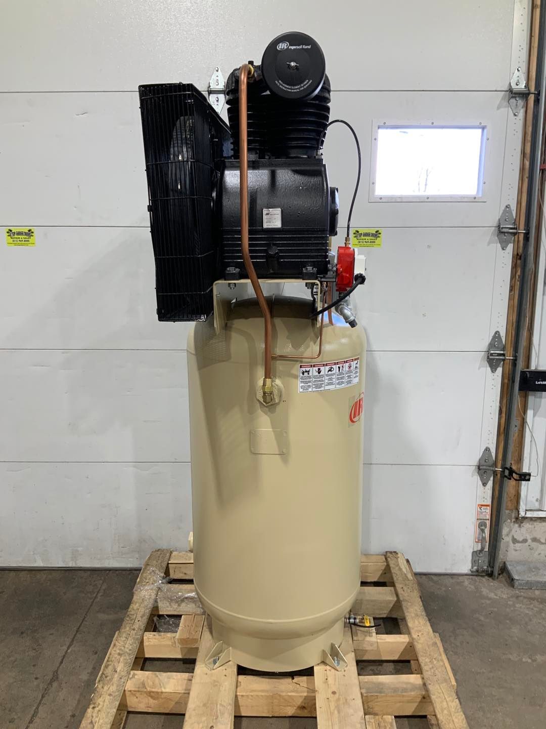 A large air compressor is sitting on a wooden pallet in front of a garage door.