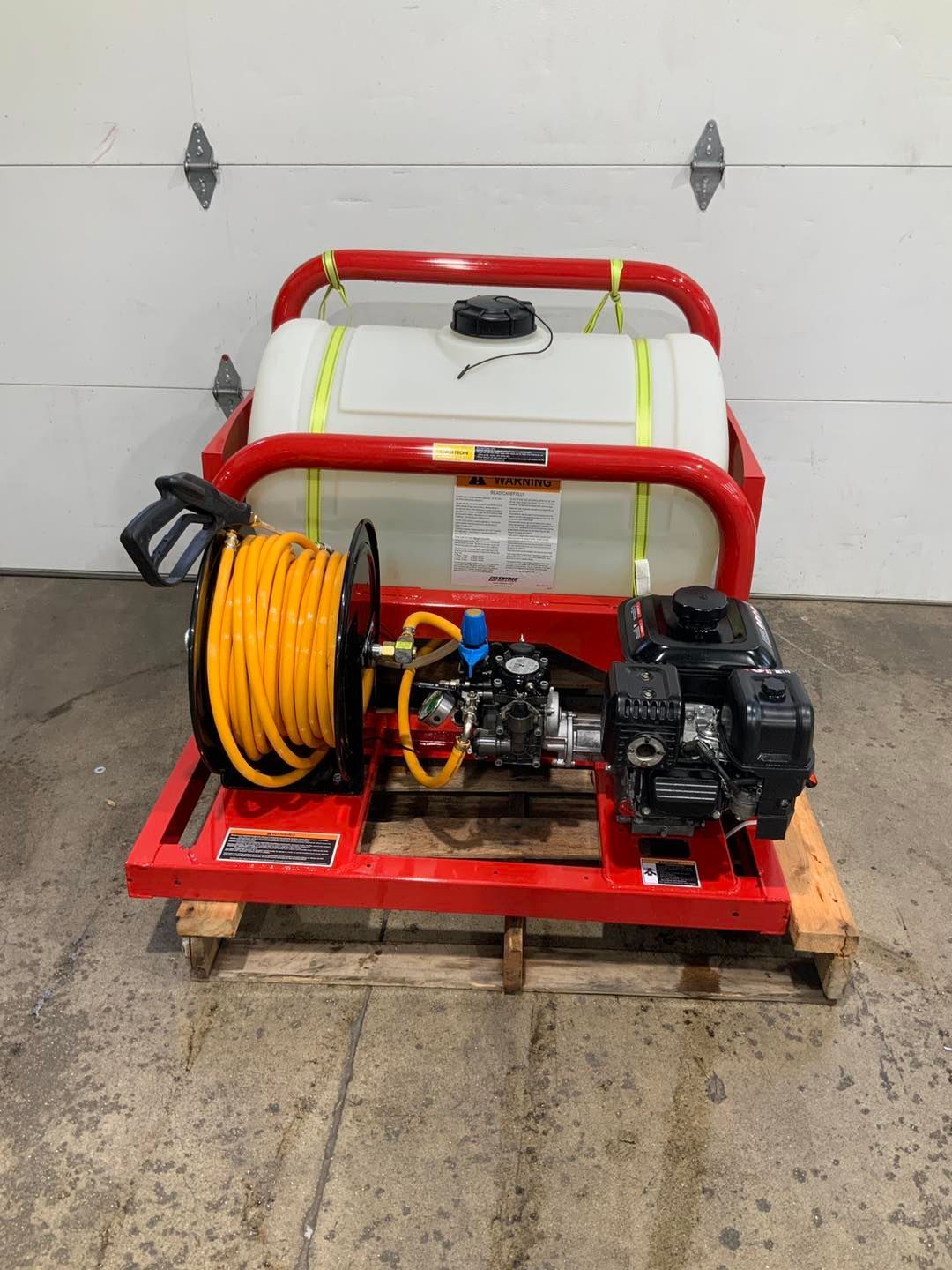 A machine with a hose attached to it is sitting on a pallet in front of a garage door.