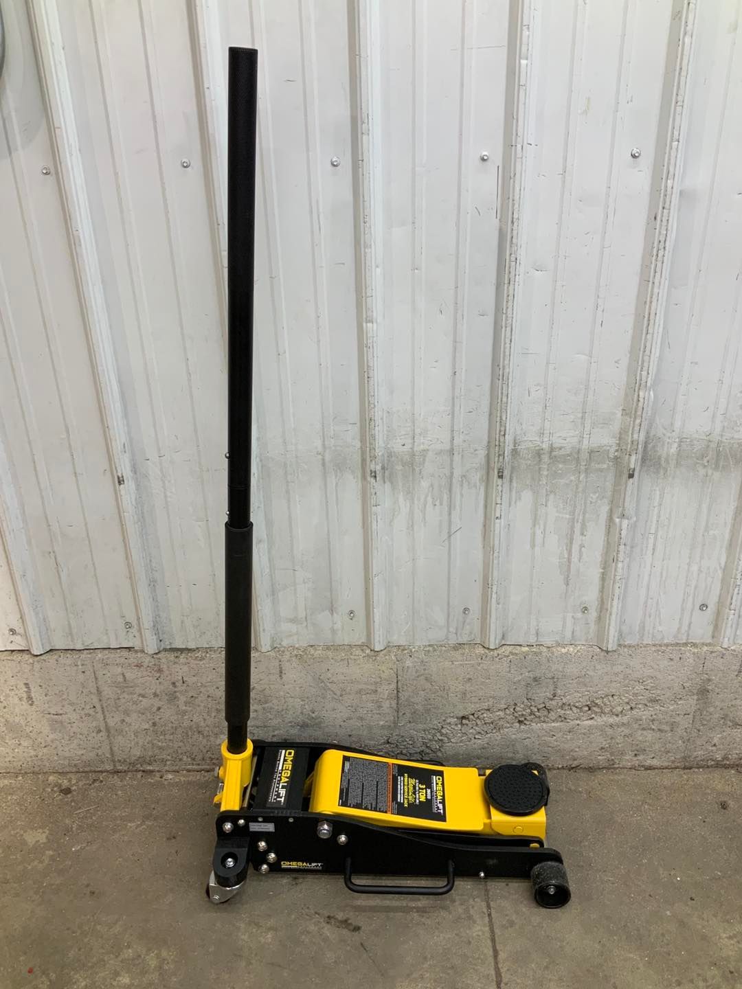 A yellow and black floor jack is sitting on the ground in front of a building.