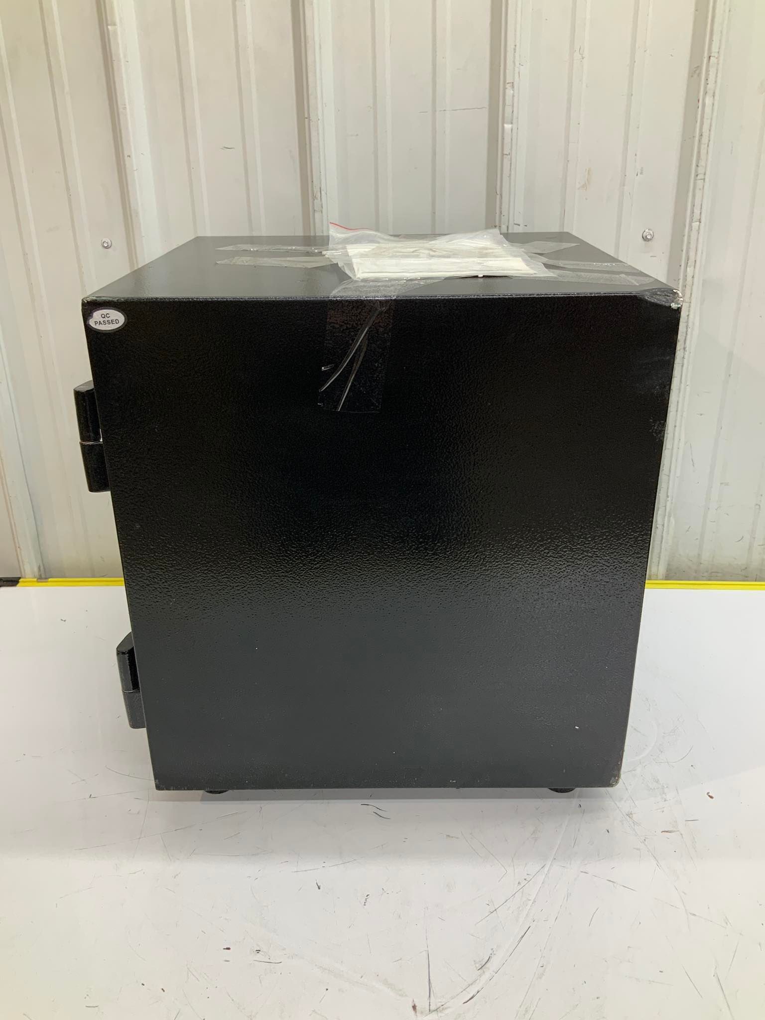 A black safe is sitting on a white table in front of a white wall.