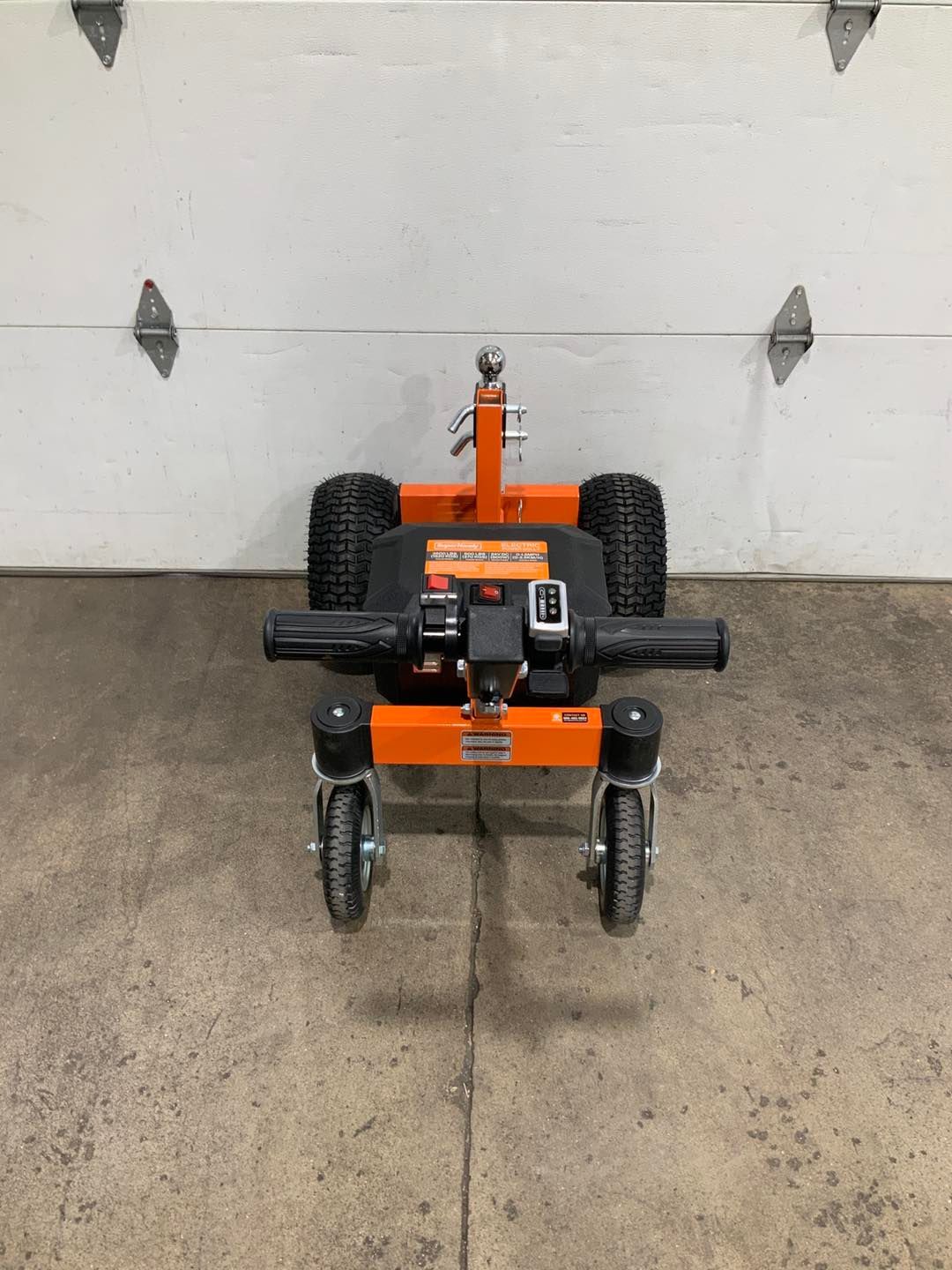 A small orange tractor is parked in front of a garage door.