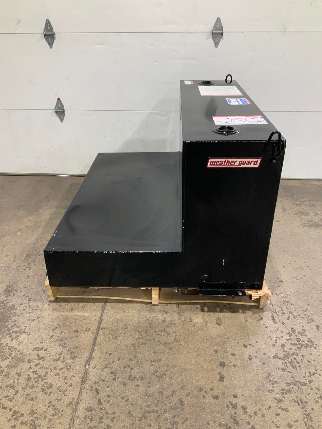 A black tank is sitting on a wooden pallet in front of a garage door.