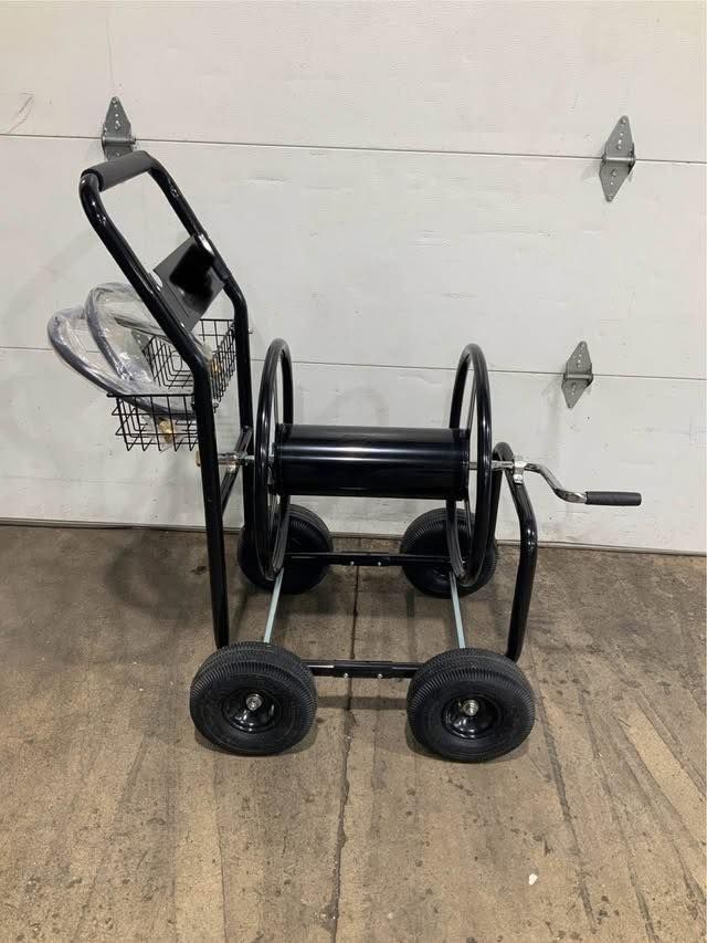 A hose reel on wheels is sitting on a wooden floor in front of a garage door.