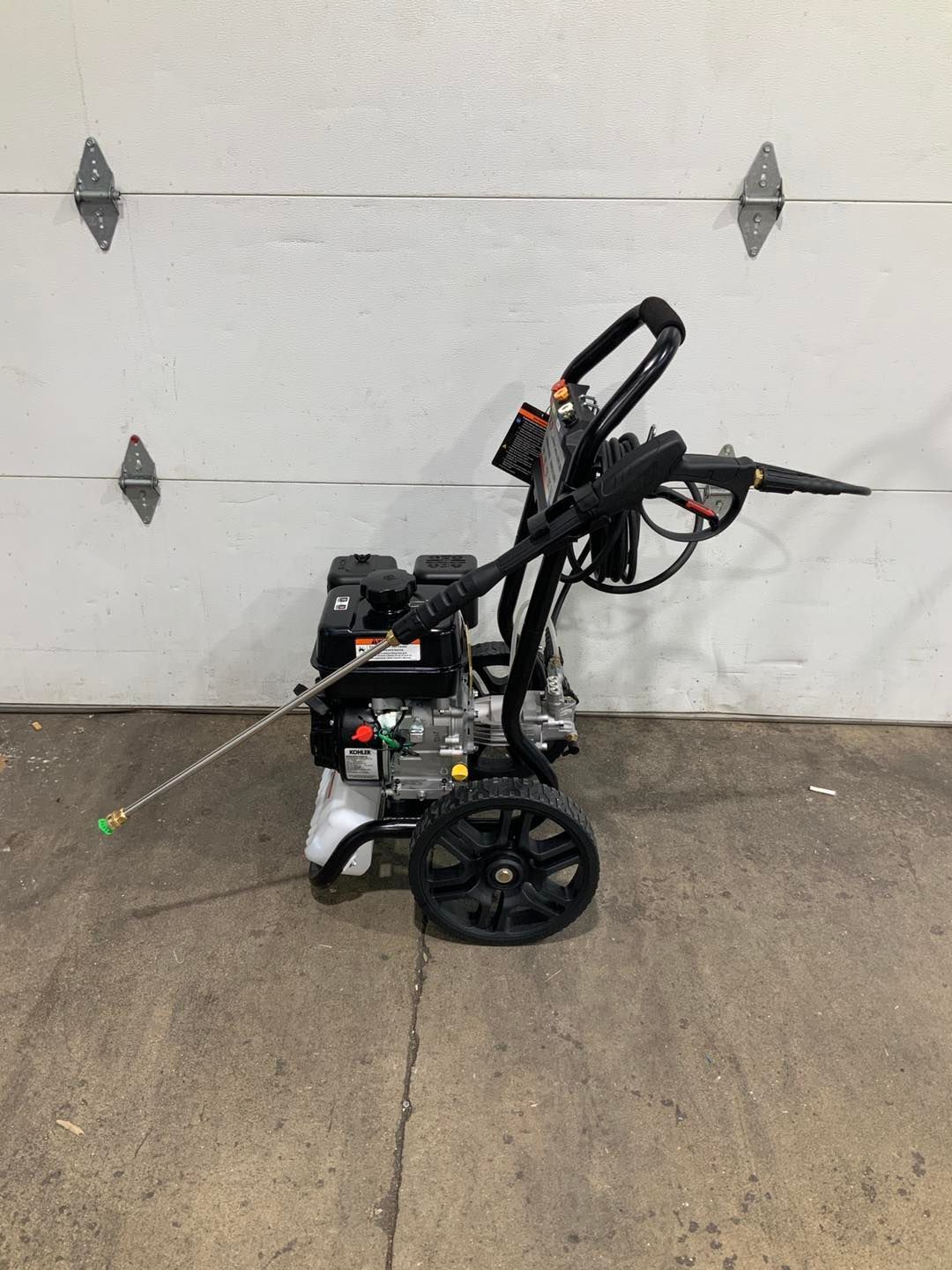 A pressure washer is sitting on the ground in front of a garage door.