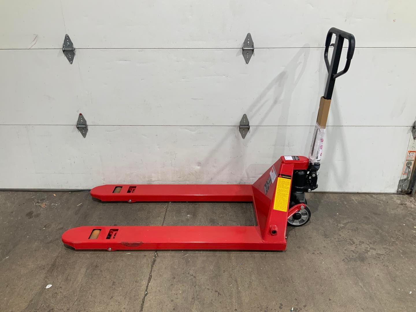 A red pallet truck is sitting in front of a garage door.