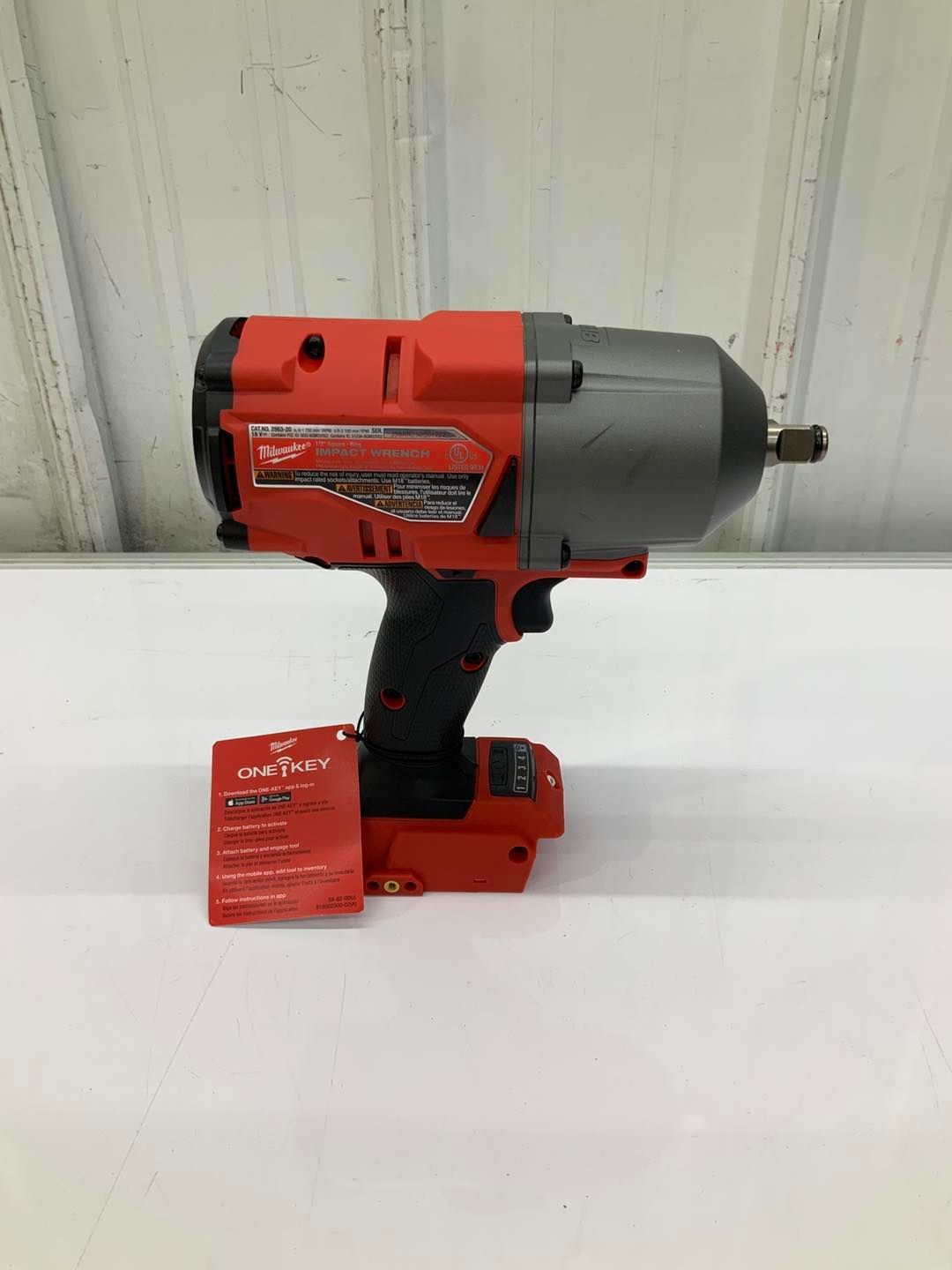 A red and black cordless impact wrench is sitting on a white table.