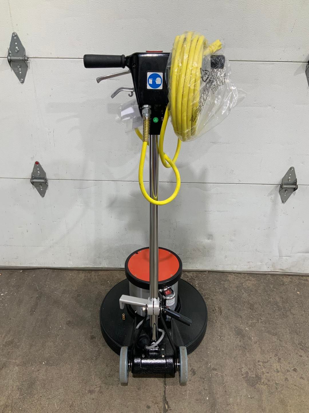 A machine with a hose attached to it is sitting in front of a garage door.