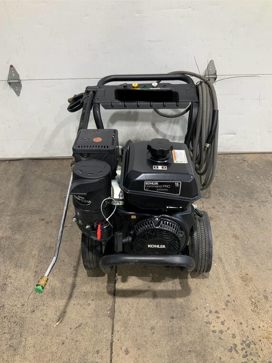 A gas powered pressure washer is sitting on the ground in front of a garage door.