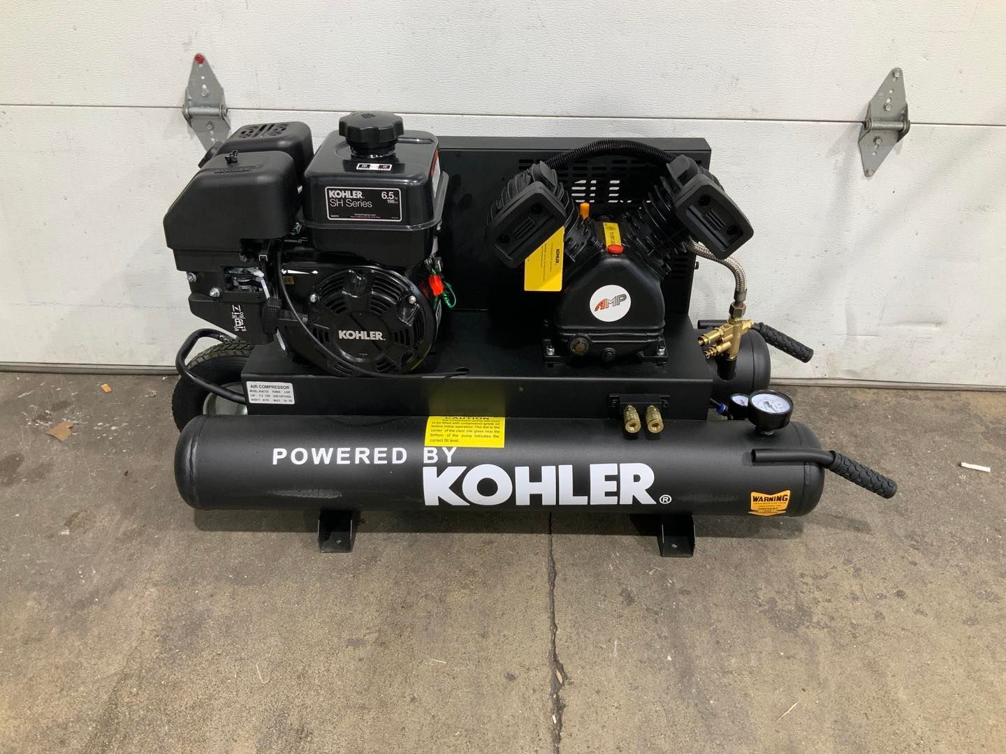A kohler air compressor is sitting in front of a garage door.