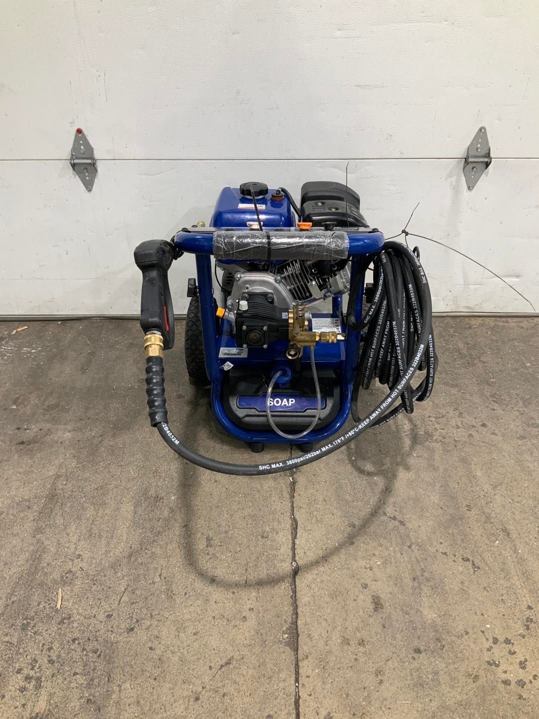 A blue pressure washer is sitting on the ground in front of a garage door.