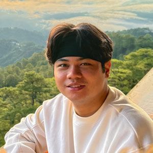 A man wearing a headband and a white sweater is sitting on a balcony.