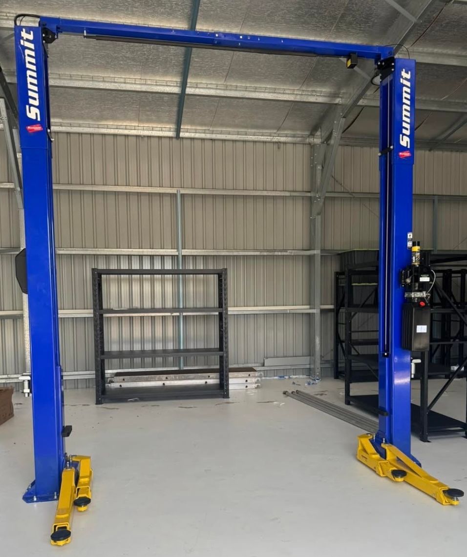 Blue car lift in an empty garage or workshop with a metal shelving unit in the back.