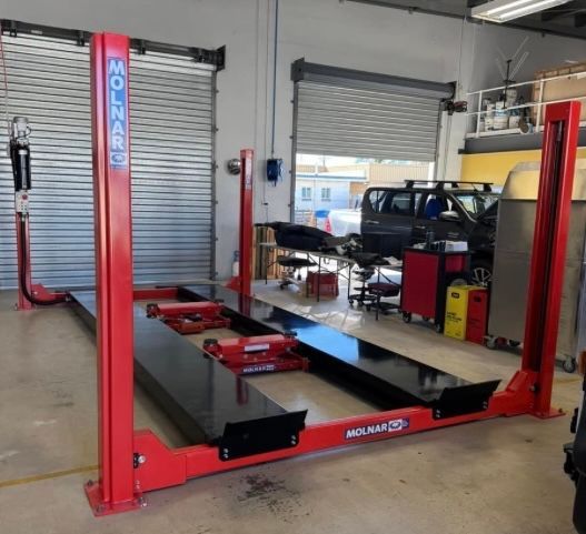 Red two-post vehicle lift in an auto shop garage with worktables and equipment in the background