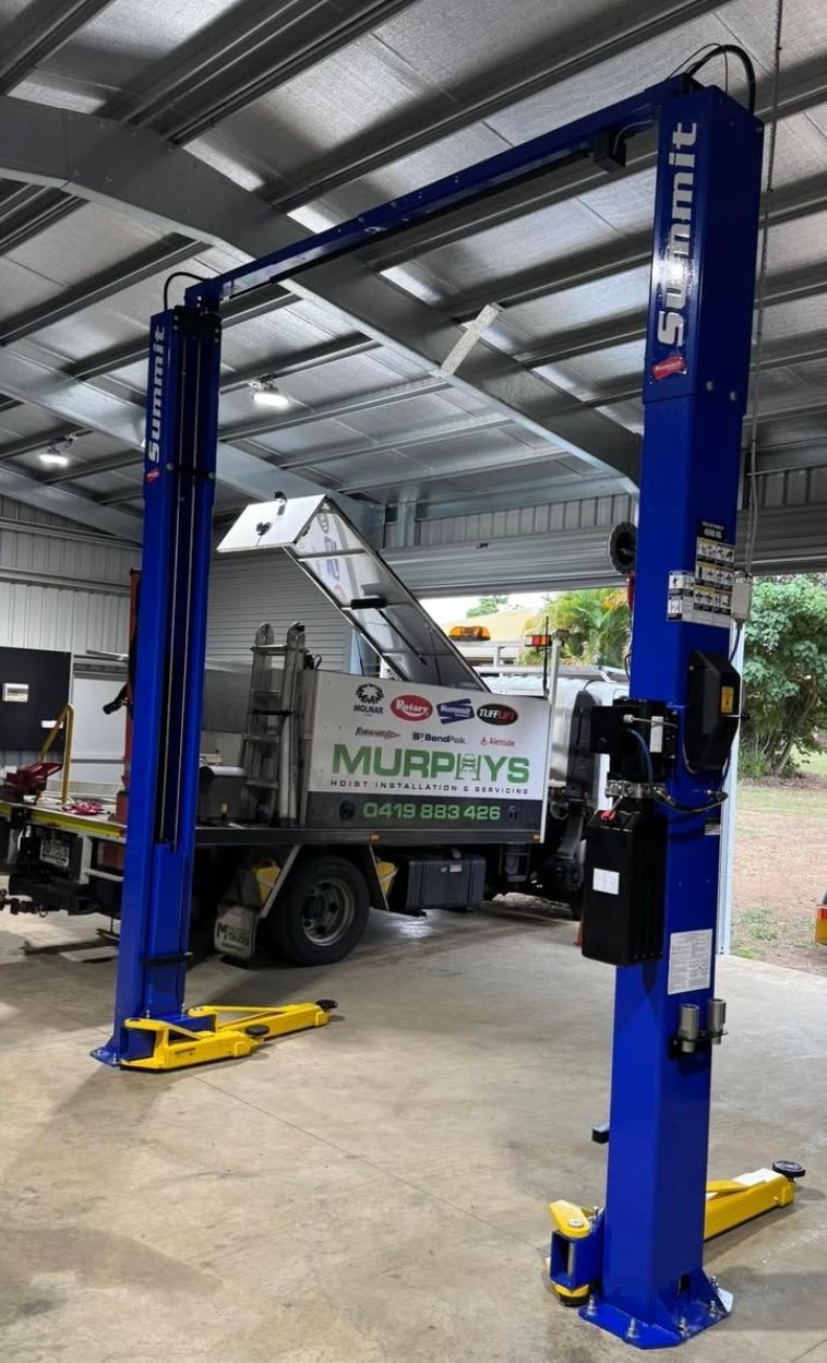 Blue four-post vehicle lift in a garage, with a utility truck parked underneath.