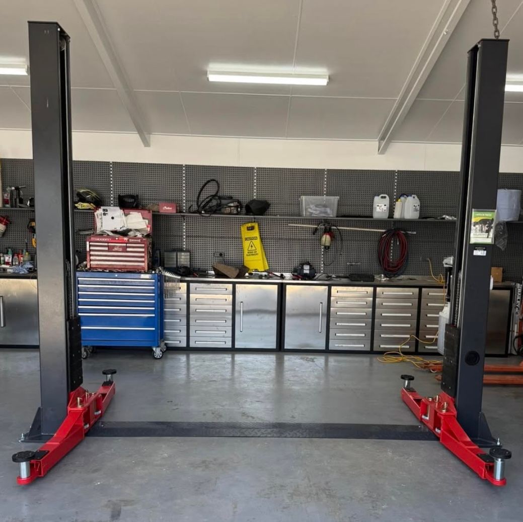 Empty two-post car lift in a clean garage with tool cabinets and equipment along the back wall