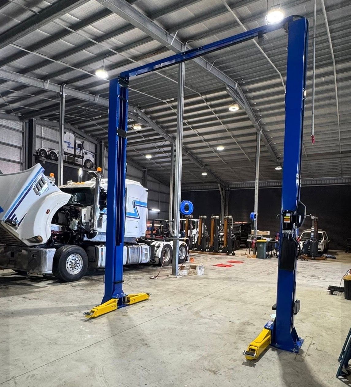 Blue two-post car lift in a large auto shop with a truck and other equipment in the background