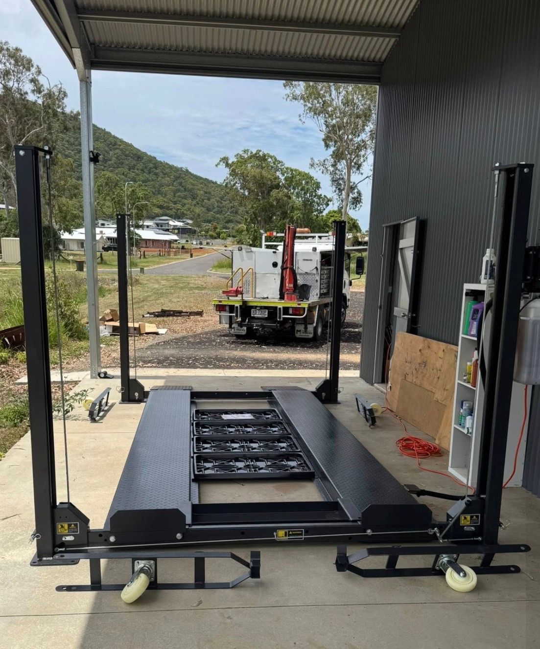 Foldable platform lift in a shed, with a truck and hillside visible outside.