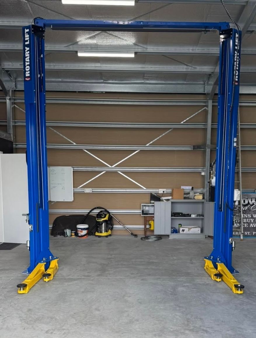 Blue two-post vehicle lift in an empty garage bay with yellow feet