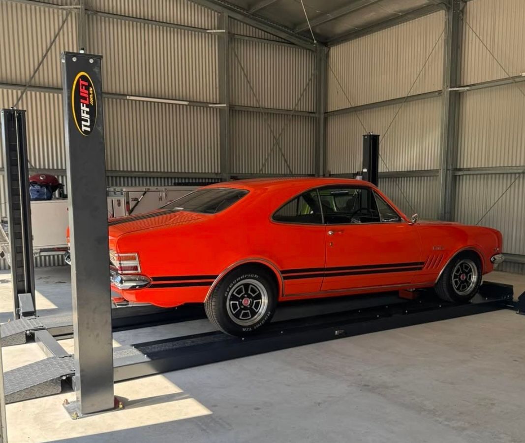 Orange classic car on a vehicle lift inside a metal garage